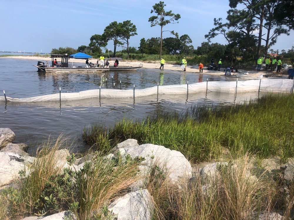 A shoreline clean-up team installs a temporary fence lined with sorbent material
