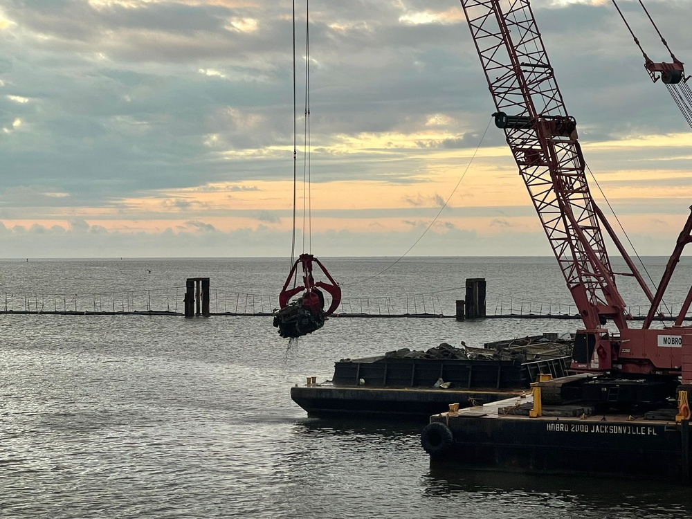 A crane operator lifts a section of a vehicle during debris removal operations