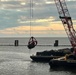 A crane operator lifts a section of a vehicle during debris removal operations