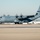 Kentucky Air Guard enters new era with arrival of C-130J Super Hercules aircraft A U.S. Air Force C-130J Super Hercules military transport aircraft is taxiing on a flight line or tarmac. The aircraft bears the tail number 85921 and a 'Kentucky' unit designation with a blue stripe, indicating it belongs to the Kentucky Air National Guard. A single airman in camouflage uniform is standing on the tarmac, likely serving as a ground guide.