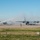 Kentucky Air Guard enters new era with arrival of C-130J Super Hercules aircraft Two U.S. Air Force C-130 Hercules military transport aircraft are receiving a traditional water cannon salute on an airfield tarmac. Two red fire trucks, numbered 65 and R-54, are positioned on either side of the aircraft, spraying arching streams of water over them. This ceremonial event likely marks a retirement, final flight, or significant milestone for the aircraft or crew.