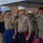 A formal military ceremony featuring United States Marine Corps and Navy personnel standing at salute under a tent canopy. Multiple officers in dress uniforms with service ribbons and rank insignia are prominently visible in the foreground. The setting appears to be an official military event, likely a change of command, retirement, or commemorative ceremony.