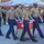 A group of U.S. Marines in dress uniform (Service Charlie/Alpha) are participating in a formal military ceremony or parade. Several Marines in the foreground are carrying a large draped object on a wheeled cart, while additional Marines stand in formation in the background. The setting appears to be an outdoor parade deck or courtyard at a Marine Corps installation.