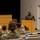 Concept to capability: Naval Warfighting Symposium A military officer in camouflage uniform stands at a wooden podium addressing a seated audience of fellow service members in a briefing or conference room setting. The audience, wearing matching camouflage uniforms, is seated in rows facing the speaker. The setting appears to be a formal military briefing or training session held in an auditorium-style room.