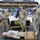 New York Jets Salute to Service Game 11/14/21 Three U.S. Army soldiers in OCP (Operational Camouflage Pattern) uniforms are staffing a recruitment and healthcare information booth at what appears to be an NFL New York Jets game tailgate or fan event. The booth promotes 'healthcare.goarmy.com' and features training mannequins dressed in military uniforms on the ground, likely used for medical/combat casualty care demonstrations. A black-draped table with Army branding and informational materials is visible in the background.