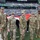 New York Jets Salute to Service Game 11/14/21 A group of U.S. Army soldiers in OCP (Operational Camouflage Pattern) uniforms stand on the field at MetLife Stadium during a pre-game ceremony, holding a large American flag. The scoreboard displays 'Countdown to Kickoff' with 17:12 remaining, and a 'Black Knights' banner is visible, suggesting an Army football game. Navy personnel in dress whites are also visible in the background participating in the flag ceremony.