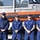 New York Jets Salute to Service Game 11/14/21 Four U.S. Coast Guard personnel in navy blue uniforms are standing in front of a U.S. Coast Guard vessel, which is mounted on a trailer. The personnel are posing for a formal group photo, with name tags visible on three of them reading 'Corwin,' 'Bohannon,' and 'Flynn.' The boat displays the distinctive orange and white U.S. Coast Guard color scheme with bold lettering.
