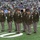 New York Jets Salute to Service Game 11/14/21 A group of U.S. Army soldiers in Army Service Uniforms (ASUs) stand in formation on the field of MetLife Stadium during what appears to be a pre-game or halftime military appreciation ceremony. The soldiers are wearing olive green dress uniforms with various rank insignia, medals, and unit patches visible. The stadium is filled with spectators in the background, and CBS Sports Network branding is visible on signage.