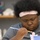 Navy Wounded Warriors Take Part in Ceramics in Honor of Warrior Care Month A young person with a natural afro hairstyle and a pink headband is focused intently on painting a small figurine or ceramic object. They are holding a fine-tipped paintbrush with a blue and gold handle, applying paint with careful concentration. The setting appears to be a classroom or art studio environment.