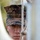 A U.S. Marine in MARPAT woodland digital camouflage uniform and cover (cap) is focused intently on working with rope or cordage, likely tying a knot or rigging equipment. The image is shot through blurred foreground elements, creating a framed, close-up perspective on the subject's face and hands. The expression is serious and concentrated.