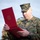 A U.S. Marine in MARPAT woodland camouflage uniform is reading from an open red presentation folder or award case. The name tape on his uniform reads 'KRAUSE' and he is wearing U.S. Marines branch tape. The setting appears to be an outdoor military ceremony.