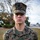 A young U.S. Marine in MARPAT woodland digital camouflage uniform stands at attention outdoors. Name tape reads 'KAUTZER' on the left chest and 'U.S. MARINES' on the right. The subject has a serious, composed expression consistent with a formal or semi-formal military portrait.