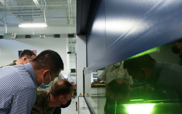 PIF Tour attendees view a laser cutter through glass
