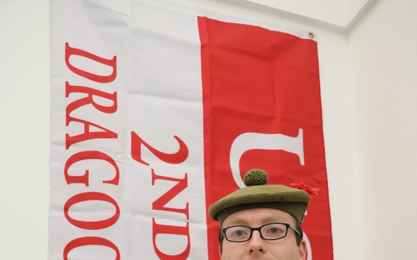 A soldier wearing British Army MultiTerrain Pattern (MTP) camouflage uniform stands with arms crossed in front of a regimental banner. The name tape on his uniform reads 'WEIR' and he is wearing a Glengarry bonnet with a green toorie, indicative of a Scottish regiment. The banner behind him reads '2ND DRAGOONS', referring to the Royal Scots Greys or Royal Scots Dragoon Guards.