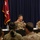 A U.S. Army panel discussion or town hall meeting is taking place with senior officers seated at a table addressing an audience of soldiers. The central figure, identified by a name placard as 'Joseph Ryan' with the title 'Commanding General &amp; Commander of Command,' is speaking into a microphone. A one-star general flag (Brigadier General flag) is visible in the background, and another placard identifies 'Col. Daniel Misigov, US Army Garrison Hawaii Commander.'
