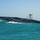 A high-speed unmanned surface vessel (USV) named 'MANTAS' is photographed underway on turquoise open water. The sleek, dark-hulled craft features a distinctive geometric camouflage pattern and an elevated sensor/camera mast mounted amidships. The vessel appears to be traveling at speed, generating a visible wake.