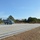 FARP Fleet Battle Problem 21-3 A military helicopter, appearing to be a Sikorsky SH-60 Seahawk in gray naval livery, is parked on a concrete landing pad surrounded by trees and dry grass. Several personnel in military flight suits are visible on and around the pad, with one individual in the foreground appearing to signal or photograph the aircraft. The setting appears to be a forward operating or training landing zone in a wooded area.