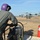 FARP Fleet Battle Problem 21-3 Military personnel are conducting a forward area refueling point (FARP) operation for a helicopter, likely an MH-60 Seahawk, on an open field. A crew member wearing a purple flight helmet and olive flight suit operates a fuel pump in the foreground, while other personnel manage the fuel hose connected to the aircraft in the background. A red fire extinguisher is prominently positioned nearby as a safety precaution during the refueling operation.