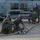 FARP Fleet Battle Problem 21-3 Military personnel from Helicopter Maritime Strike Squadron 72 (HSM-72) are conducting hot refueling operations on what appears to be an MH-60R Seahawk helicopter on a flight line or tarmac. Ground crew members wearing purple cranials (helmets) are managing a fuel hose while another crew member in a white helmet observes near the aircraft. The scene appears to be taking place during low-light conditions, likely dawn or dusk.