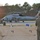 FARP Fleet Battle Problem 21-3 A U.S. Navy MH-60R Seahawk helicopter assigned to HSM-72 (Helicopter Maritime Strike Squadron 72), tail number 704, is on a tarmac being serviced or refueled by ground crew personnel. Multiple personnel in olive drab flight suits are working around the aircraft, while a forward observer or coordinator stands in the foreground near a tan canvas barrier. The scene appears to be a forward arming and refueling point (FARP) operation during low-light conditions, likely at dusk or dawn.