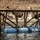 U.S. service members train in French Desert Commando Course in Africa Military personnel in camouflage uniforms are navigating a water-based obstacle course, traversing horizontal bars on a wooden frame structure mounted on floating blue barrels. At least three individuals are visible in various stages of crossing the obstacle, with water splashing below them. The number '2020' is painted on the blue barrel float platform, and a yellow kayak is visible to the right.