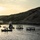 U.S. service members train in French Desert Commando Course in Africa A calm body of water at sunset or sunrise, set against arid, rocky hillsides. Several floating structures made of wood and barrels are anchored in the water, suggesting a water park or recreational obstacle course. A small inflatable motorboat with several people aboard is visible in the foreground.