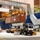 A busy container port terminal captured during nighttime or indoor-lit operations, showing a ship-to-shore crane unloading ZIM shipping containers from a large cargo vessel. A terminal tractor (yard truck) numbered 14048 is positioned beneath the crane on lane 35, ready to receive containers. Multiple workers, vehicles, and stacked containers are visible in the background, indicating active port operations.