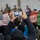 Celebrating the New Year at Task Force Liberty A person holds up a smartphone to photograph or record a gathering inside what appears to be a large tent or temporary facility. Both a United States flag and an Afghan flag are visible in the background, along with a crowd of people and individuals wearing face masks. The scene suggests a formal or organized event involving Afghan evacuees or refugees, likely at a military or transit facility.