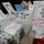 Celebrating the New Year at Task Force Liberty A display table covered with a polka-dot tablecloth showcases artwork created by guests, with a bilingual sign in English and what appears to be Dari/Farsi instructing viewers not to touch the pieces. The artwork includes pencil portraits, colorful paintings, and drawings arranged along the table. A header on the sign reads 'Better Every Day!' suggesting this may be part of a shelter or community support program.