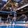 USAFA Men's Basketball Vs Utah State A college basketball game is being played at the Air Force Academy's Clune Arena, home of the Falcons. An Air Force player in a gray and blue uniform is executing a layup at the basket while opposing players wearing dark uniforms with the letter 'U' (likely Utah State) look on. The arena is partially filled with spectators and features prominent 'AF' and 'Air Force Basketball' branding throughout.