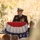 A senior U.S. Navy officer in dress uniform stands at a podium draped with a patriotic red, white, and blue bunting, delivering a speech at what appears to be an outdoor military ceremony. Multiple service medals and ribbons are visible on his uniform, indicating significant rank and service. A second uniformed military officer is visible in the background to the right.