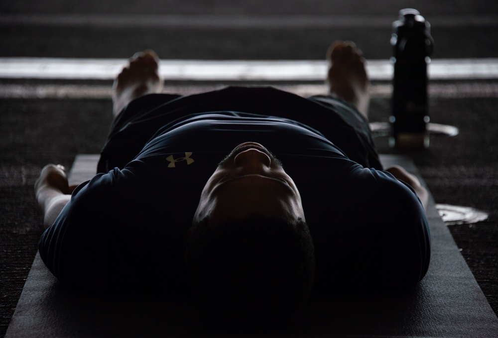 Sailors participate in a yoga class in the hangar bay of USS Carl Vinson