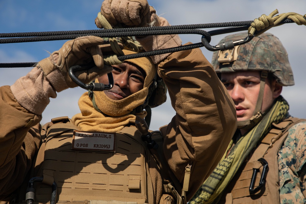 Marine engineers and Navy Seabees construct a one rope bridge during Winter Pioneer 22