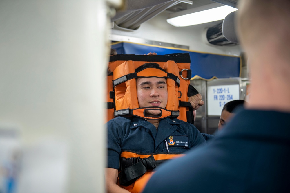 Sailor acts as simulated patient during a stretcher bearer trainign course aboard USS Gonzalez.