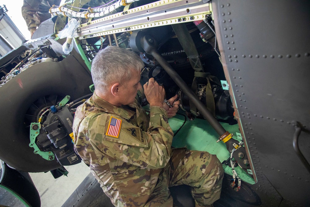 A Soldier installs a generator on an AH-64 Apache helicopter