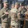 Kentucky Guardsmen Assume Authority A group of U.S. Army soldiers in OCP (Operational Camouflage Pattern) uniforms are participating in a military ceremony, likely a casing or uncasing of colors. Soldiers are handling a furled unit guidon or colors with gold fringe, mounted on a staff. The ceremony appears to be taking place outdoors at a military installation.