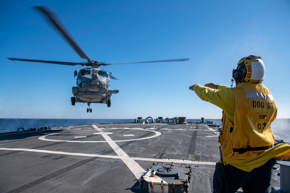 Boatswain’s Mate 3rd Class Tra’shaun Cooper, from Homestead, Texas, directs a MH-60R Sea Hawk helicopter