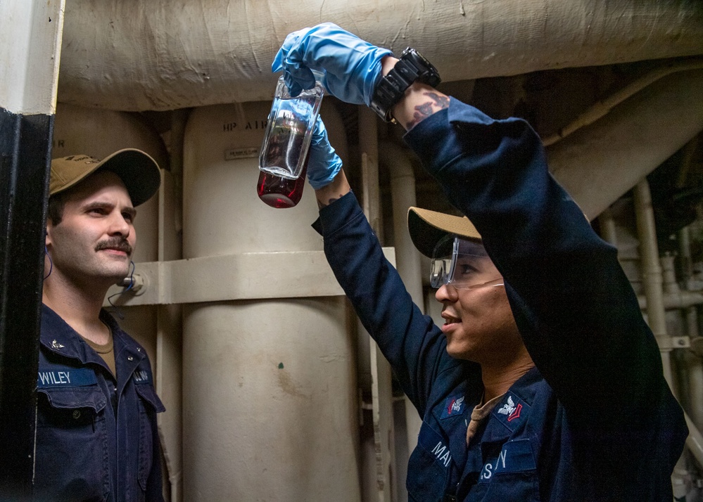 Gas Turbine Systems Technician (Mechanical) Dylan Mai (right), from Los Angeles, Calif., verifies an oil sample is clear and bright with Gas Turbine Systems Technician (Electrical) 3rd Class Zachary Wiley (left), from Lufkin, Texas