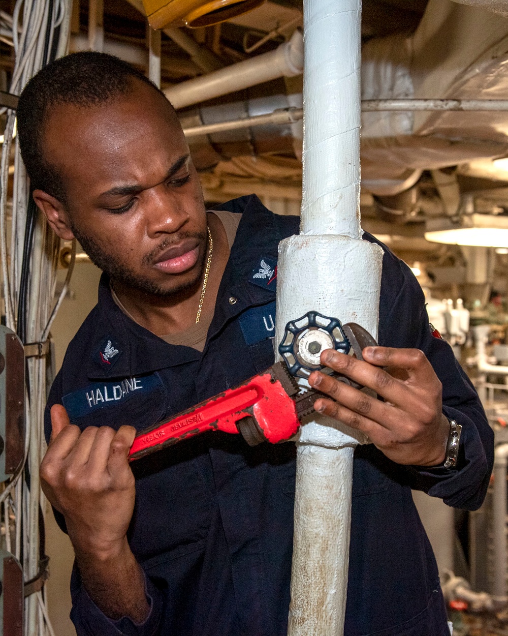 Machinist Mate 3rd Class Andre Haldane, from Philadelphia, Pa., tightens a valve in an engineering space