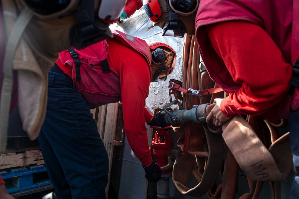 Sailors connect a y-gate to a fire hose station, during a firefighting drill