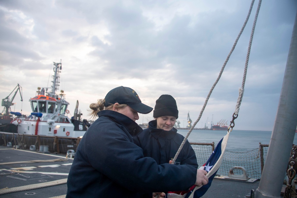 Hospital Corpsman 2nd Class Madyson, Schmidt, left, from Ravenna, Neb., and Fire Controlman (AEGIS) 2nd Class Abby Wilson, from Golden, Colo., prepare to raise the national ensign