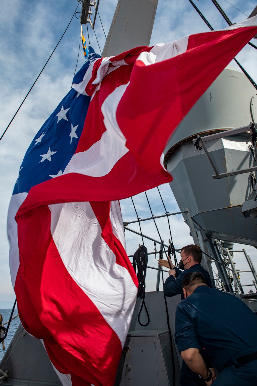 Quartermaster 2nd Class Dylan Stevens, top, from Irvine, Ky., and Quartermaster Seaman Gonzalo Pinedafausto, bottom, from Los Angeles, Calif., haul up the battle ensign