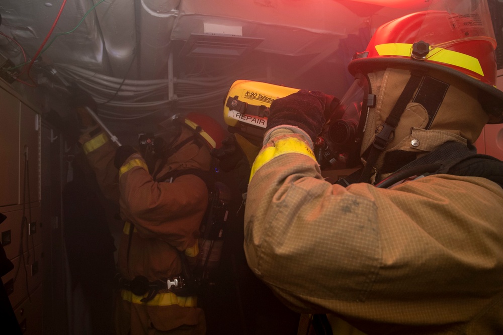 Sailors conduct overhaul of a simulated fire with a rake and Naval Firefighter Thermal Imager during a firefighting drill