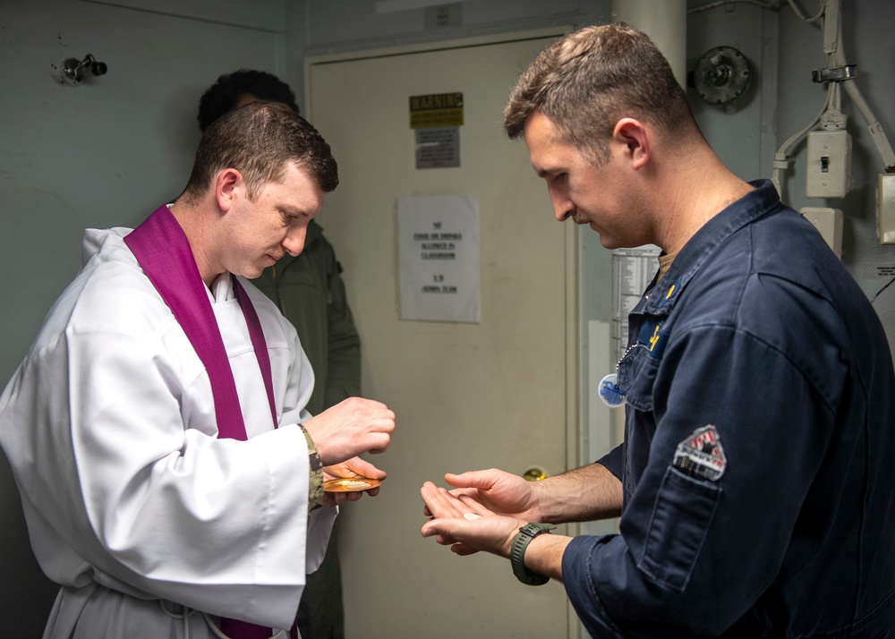 Lt. Fr. Rene Pellessier, left, from Lafayette, La., assigned to Nimitz-class aircraft carrier USS Dwight D. Eisenhower (CVN 69) offers communion to Ensign Matthew Webber, from York, Maine, during a Catholic mass