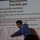A presenter is delivering a lecture or conference talk about 'Assumptions: End-tidal gas' with a focus on aerospace counter-examples. The speaker is pointing at a projected slide that discusses mask leaks diluting gas samples, accompanied by a CO2 tracing graph labeled 'MBU 23/P'. The presentation appears to be a technical or scientific talk related to aerospace physiology or respiratory gas analysis.