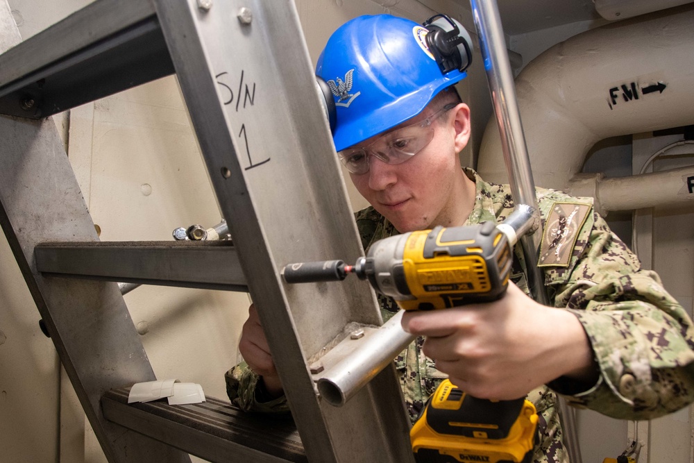 Sailors performs maintenance on ladderwell