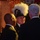 Commander, 7th Fleet Attends Surface Warfare Officer's Ball Three men in dark formal attire are engaged in conversation at what appears to be a formal event or ceremony. The central figure is wearing a distinctive ceremonial bicorne-style hat with white feather plumes and an emblem or badge on the front. The setting features warm ambient lighting with string lights and draped fabric in the background.