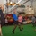 The Harry S. Truman Carrier Strike Group is on a scheduled deployment in the U.S. Sixth Fleet area of operations in support of naval operations to maintain maritime stability and security. A volleyball game is being played indoors on what appears to be the hangar deck of a U.S. Navy ship, evidenced by military signage, equipment, and unit markings (HSM-72) visible in the background. Players in casual athletic wear compete at the net while a crowd of spectators watches from the sidelines. A referee in a black-and-white striped shirt and an electronic scoreboard are also visible.