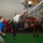 The Harry S. Truman Carrier Strike Group is on a scheduled deployment in the U.S. Sixth Fleet area of operations in support of naval operations to maintain maritime stability and security. A volleyball game is being played indoors in what appears to be a military hangar bay, likely aboard a naval vessel based on the visible signage (HSM-7, AFFF stations, hangar deck markings). A player in a white shirt is jumping to spike the ball over the net while teammates and opponents are positioned around the court. A large crowd of spectators watches from the sidelines, and a referee in a black-and-white striped shirt officiates the match.