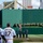 A pre-game ceremony at PNC Park in Pittsburgh, home of the Pittsburgh Pirates, featuring a military honor guard presenting the American flag and a service branch flag on the field. Two Pirates players are visible in the foreground — Hayes (#13) and Shelton (#17) — standing at attention facing the honor guard. The iconic Roberto Clemente Bridge and Pittsburgh skyline, including a Duquesne Light Co. building, are visible in the background beyond the green outfield wall.